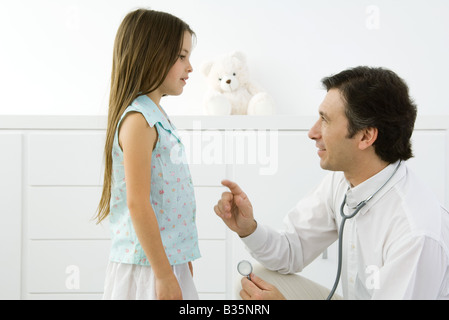 Medico accovacciato, spiegare qualcosa alla ragazza, vista laterale Foto Stock