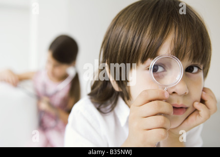 Little Boy guardando attraverso la lente di ingrandimento in telecamera Foto Stock