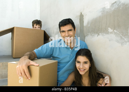 Famiglia seduti sulle scale con le scatole di cartone, ragazzo nascosto Foto Stock