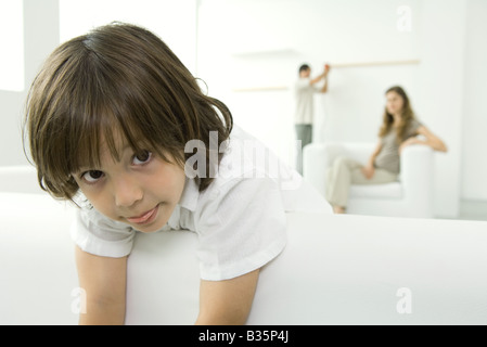 Little Boy sporgendoti lettino, con la lingua fuori a fotocamera, genitori in background Foto Stock