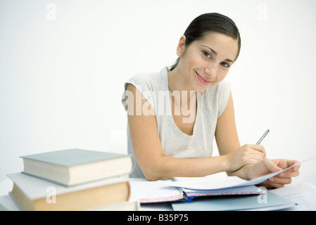 Donna che lavorano a tavola, tenendo in mano carta e penna, sorridente in telecamera Foto Stock