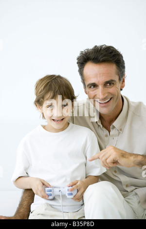 Ragazzo la riproduzione del video gioco, padre seduto con lui, puntando al controller Foto Stock