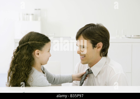 Bambina regolando il suo padre di cravatta, entrambi sorridendo a ciascun altro Foto Stock