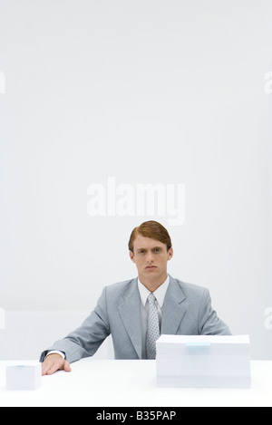 Imprenditore seduta a tavola con due differenti dimensioni delle pile di carta Foto Stock