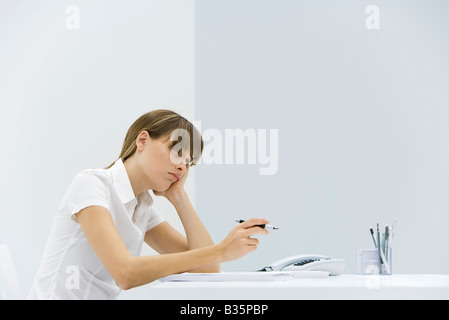 Donna seduta alla scrivania, appoggiato la testa nella sua mano, guardando lontano e accigliata Foto Stock