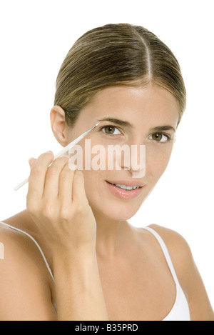 Donna applicazione di make-up occhi con pennello, guardando la fotocamera Foto Stock