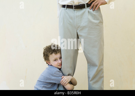 Ragazzo aggrappati al suo padre è la gamba, guardando la telecamera, vista ritagliata Foto Stock