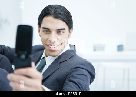 Giovane imprenditore tramite telefono cellulare per scattare foto di se stesso, sorridente Foto Stock