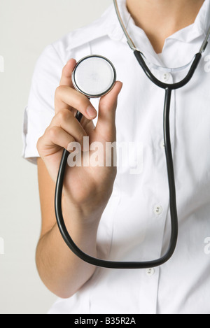 Medico tenendo lo stetoscopio e mostrando alla telecamera, vista ritagliata Foto Stock