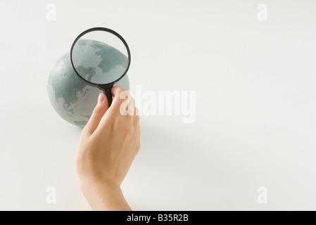 Mano che tiene la lente di ingrandimento su globo, vista ritagliata Foto Stock