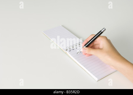 Mano che tiene la penna, pronti a scrivere nel blocco note reclinata, vista ritagliata Foto Stock