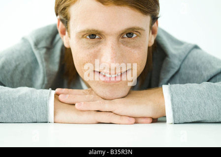 Giovane uomo appoggiato la testa su bracci ripiegati, sorridente in telecamera, ritratto Foto Stock