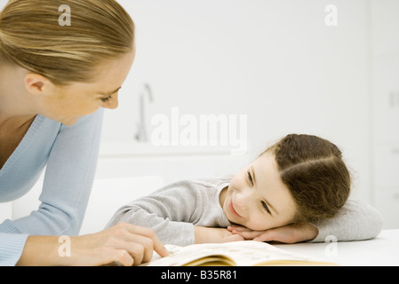 Madre e figlia sorridente ad ogni altra ragazza testa di appoggio sui bracci, donna puntando al libro Foto Stock