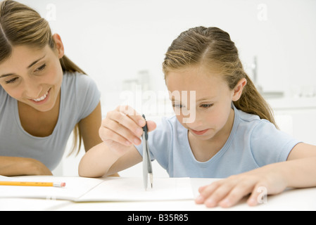 Ragazza con la bussola di fare geometria, madre guarda e sorridente Foto Stock