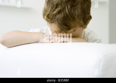 Piccolo Ragazzo seduto con la testa rivolta verso il basso sulle sue braccia Foto Stock