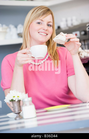 Giovane donna seduti ad un tavolo a bere un tè e mangiare un dolce trattare Foto Stock