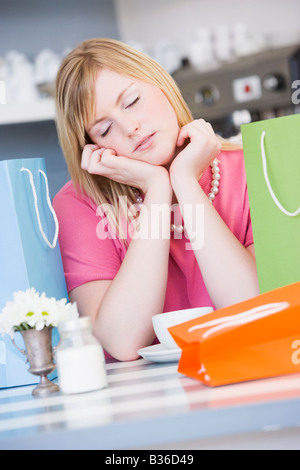 Esaurito giovane donna seduta al tavolo per una pausa dallo shopping Foto Stock