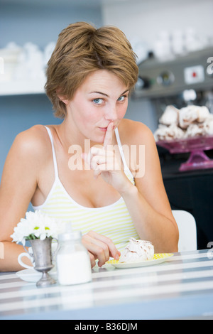 Giovane donna seduti ad un tavolo a bere un tè e mangiare un dolce trattare Foto Stock