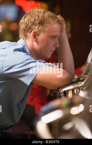 Uomo in casino Gioca slot machine frustrati con persone di background (messa a fuoco selettiva) Foto Stock