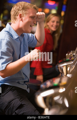 Uomo in casino Gioca slot machine sorridente con persone di background (messa a fuoco selettiva) Foto Stock