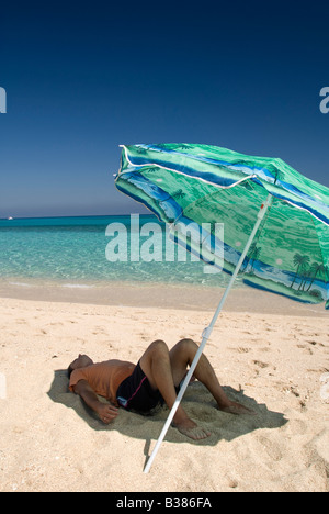 Un uomo rilassante sotto ombrellone in spiaggia Foto Stock