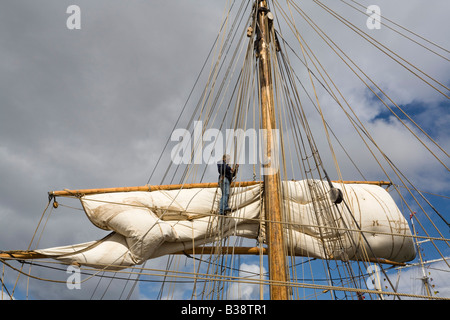 Persona le funi di smistamento e la vela in alto sulla piazza montante truccate sulla barca in Tall Ships race sailor lavorando Foto Stock