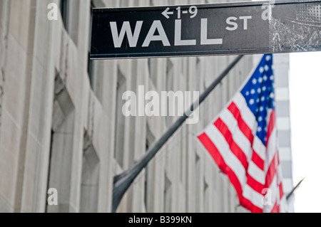 Wall Street Street Sign American Flag New York City // NEW YORK CITY, Stati Uniti - i cartelli di Wall Street si trovano all'incrocio con la bandiera americana visibile sullo sfondo. Situato nel quartiere finanziario di Manhattan, questo iconico incrocio rappresenta il cuore della finanza e del capitalismo americani. Wall Street ospita la Borsa di New York e numerose istituzioni finanziarie, che fungono sia da luogo fisico che da potente simbolo del sistema economico americano. La giustapposizione dei cartelli stradali con le stelle e le strisce sottolinea il profondo legame tra gli americani Foto Stock