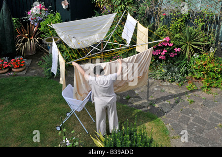 Indietro giardino & prato della proprietà residenziale vista aerea donna anziana matura appesa bagnata lavaggio sulla linea di vestiti rotativi per asciugare al sole Inghilterra UK Foto Stock