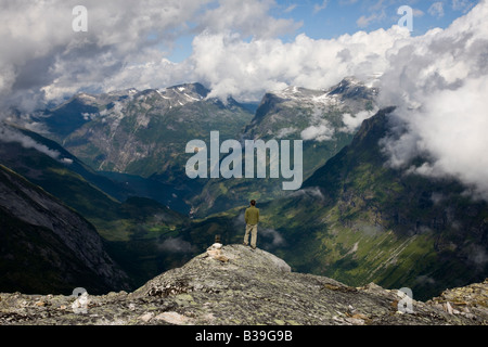 La prospettiva aerea 1 giovani adult man 20's guardando a Geiranger Fjord, Norvegia da Dalsnibba montagna altopiano, drammatica azzurro cielo, soffici nuvole Foto Stock