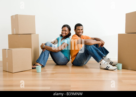 African American maschio e femmina giovane seduto sul pavimento accanto a contenitori per il trasloco Foto Stock