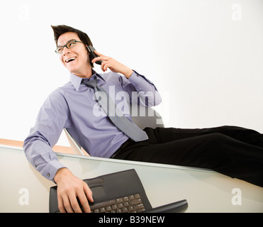 Ridendo imprenditore asiatico seduto alla scrivania parlando al cellulare Foto Stock