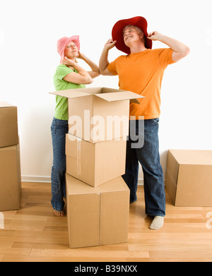 Coppia di mezza età cercando su stupidi cappelli mentre imballo o disimballaggio contenitori per il trasloco Foto Stock