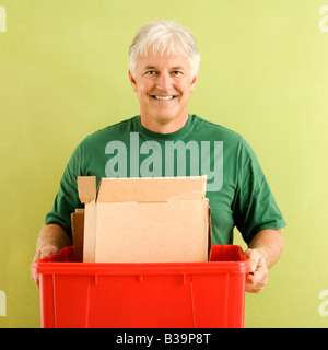 Ritratto di sorridere uomo adulto tenendo il contenitore di riciclaggio piena di cartone Foto Stock