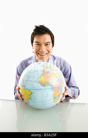 Giovane uomo asiatico seduta holding globe sorridente Foto Stock