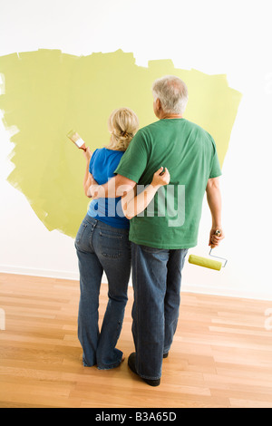 Coppia di mezza età pittura verde parete osservando il loro lavoro Foto Stock