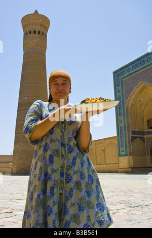 Donna con il plov davanti alla Moschea Kalon e Minareto a Bukhara Uzbekistan Foto Stock