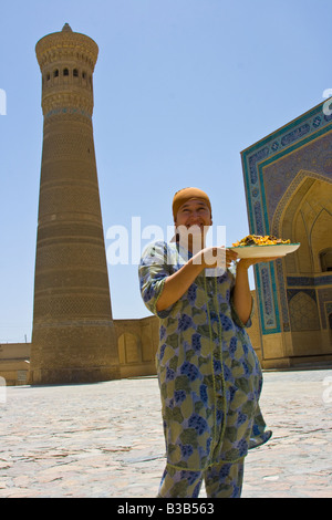 Donna con il plov davanti alla Moschea Kalon e Minareto a Bukhara Uzbekistan Foto Stock