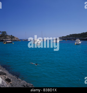 Scena in Cala Mondrago - nuotatore + barche e yacht in cerca di ancoraggio al largo - vicino a Cala D'Or, costa orientale di Mallorca. Foto Stock