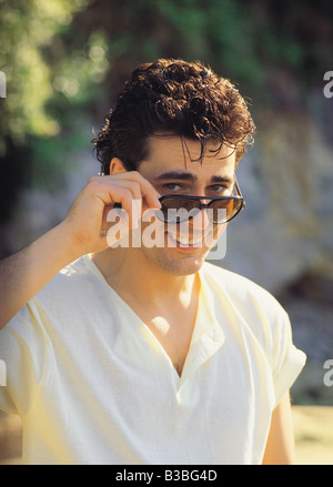 Giovane uomo all'esterno guardando sopra la parte superiore dei suoi occhiali da sole Foto Stock