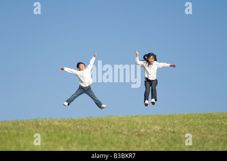 Un ragazzo e una ragazza jumping sull'erba Foto Stock
