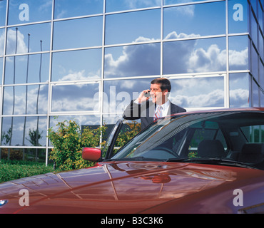 Imprenditore parlando su telefono cellulare in piedi con la vettura al di fuori ufficio edificio Foto Stock