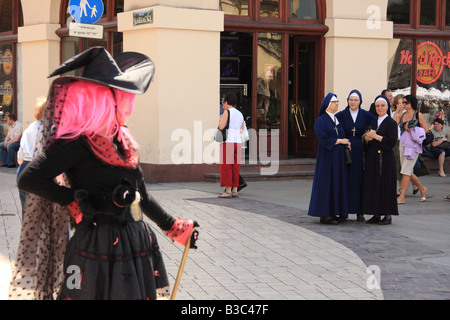 Street intrattenitore vestita come una strega, guardato da monache di Rynek Glowny (piazza del Mercato di Cracovia, Polonia Foto Stock