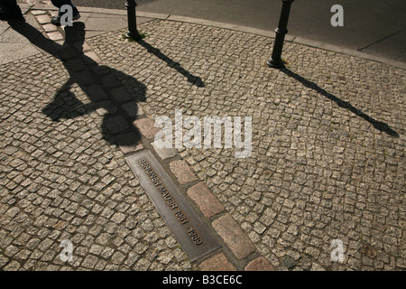 Ombra umana leggendo un libro guida che attraversano la linea simbolica del luogo in cui il Muro di Berlino era stato a Berlino, Germania Foto Stock