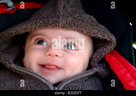 Un bambino guarda con entusiasmo come egli siede nel suo passeggino in inverno Foto Stock