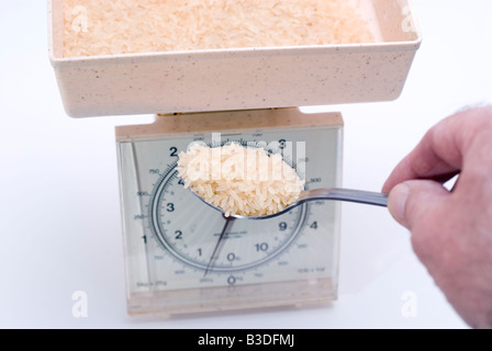 Ammucchiò cucchiaio di grana lunga riso essendo posto sulla bilancia da cucina per pesare Foto Stock