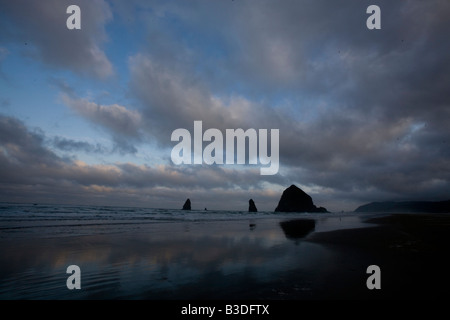Sunrise e pile di mare sulla spiaggia di Cannon Oregon con una drammatica sky in background Foto Stock