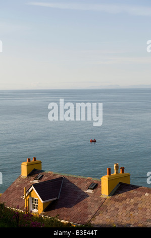 New Quay, Galles. Una vista sui tetti della città in mare con due uomini che pescano pacificamente da un piccolo gommone Foto Stock