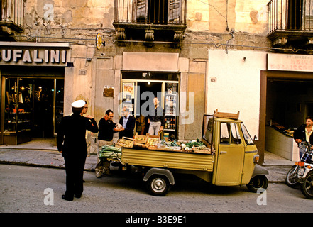 Un carrello con frutta fresca e verdura si ferma al di fuori di un negozio 4 uomini e un uomo di polizia come parte di una scena di strada a SCIACCA Foto Stock