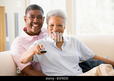Matura in soggiorno utilizzando il telecomando sorridente Foto Stock