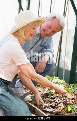 Donna in serra di piantare semi e uomo azienda annaffiatoio sorridente Foto Stock